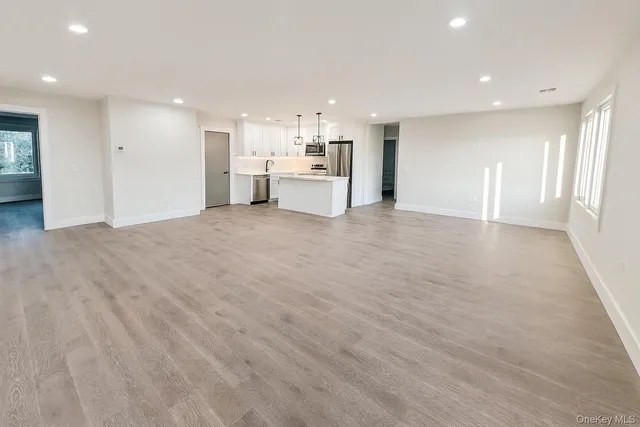a view of an empty room with kitchen and window