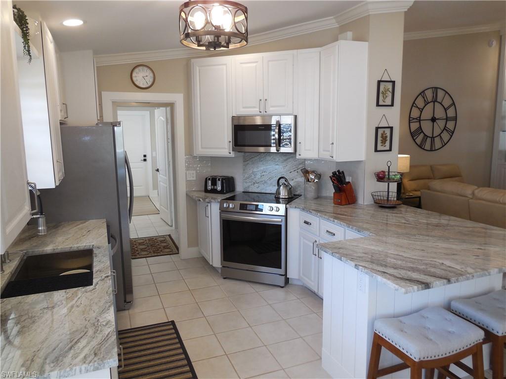 5441 Guadeloupe Way Naples, FL 34119 - Photo 11 of 45 Kitchen featuring stainless steel appliances, light tile patterned flooring, crown molding, a peninsula, and white cabinetry
