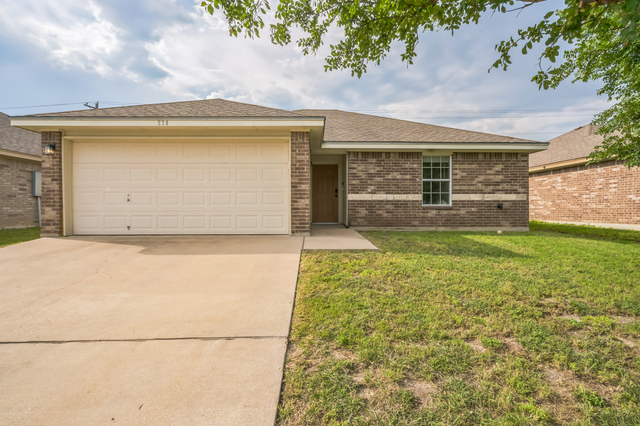 Single story home featuring concrete driveway, a garage, a front yard, brick siding, and roof with shingles