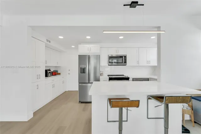 a large white kitchen with stainless steel appliances granite countertop a refrigerator and a stove top oven