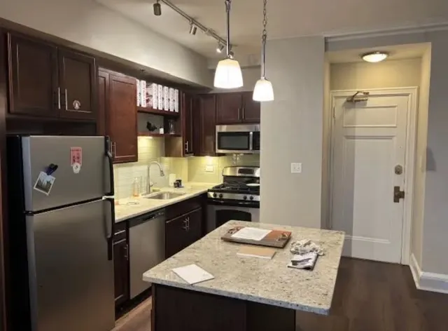 a kitchen with granite countertop a refrigerator a stove a sink a dining table and chairs with wooden floor