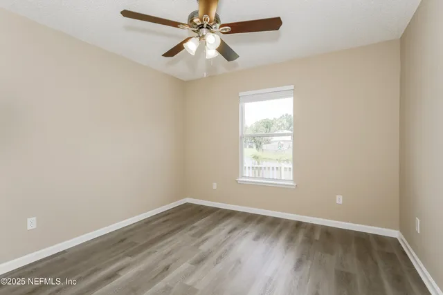 an empty room with wooden floor fan and windows