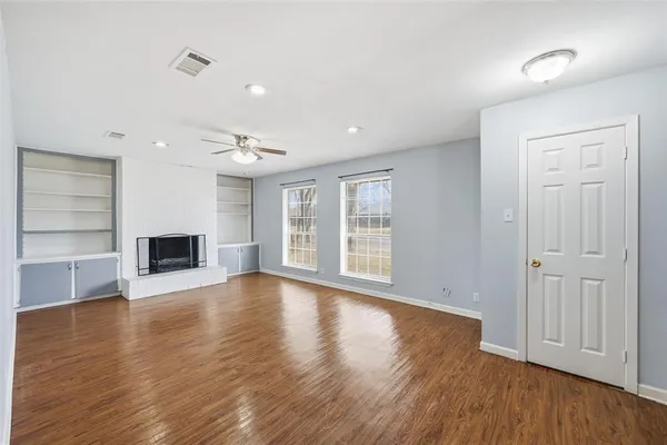 an empty room with wooden floor fireplace and windows