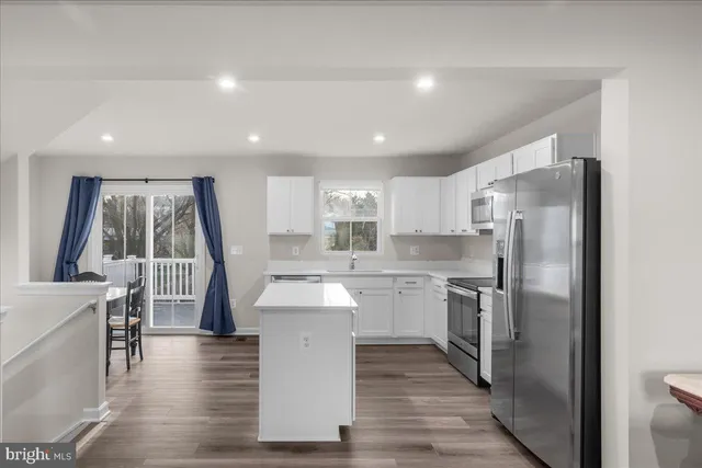 a kitchen with stainless steel appliances a refrigerator a sink dishwasher a stove with white cabinets and wooden floor