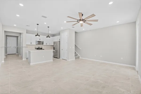 an empty room with wooden floor staircase and kitchen view