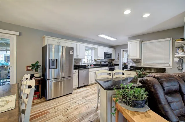 a kitchen with stainless steel appliances kitchen island granite countertop a refrigerator a stove a sink dishwasher and white cabinets with wooden floor
