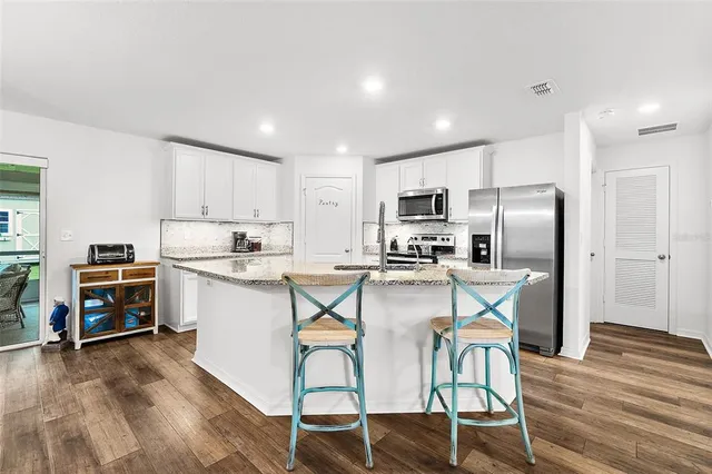 a kitchen with stainless steel appliances a stove a sink a refrigerator white cabinets and wooden floor