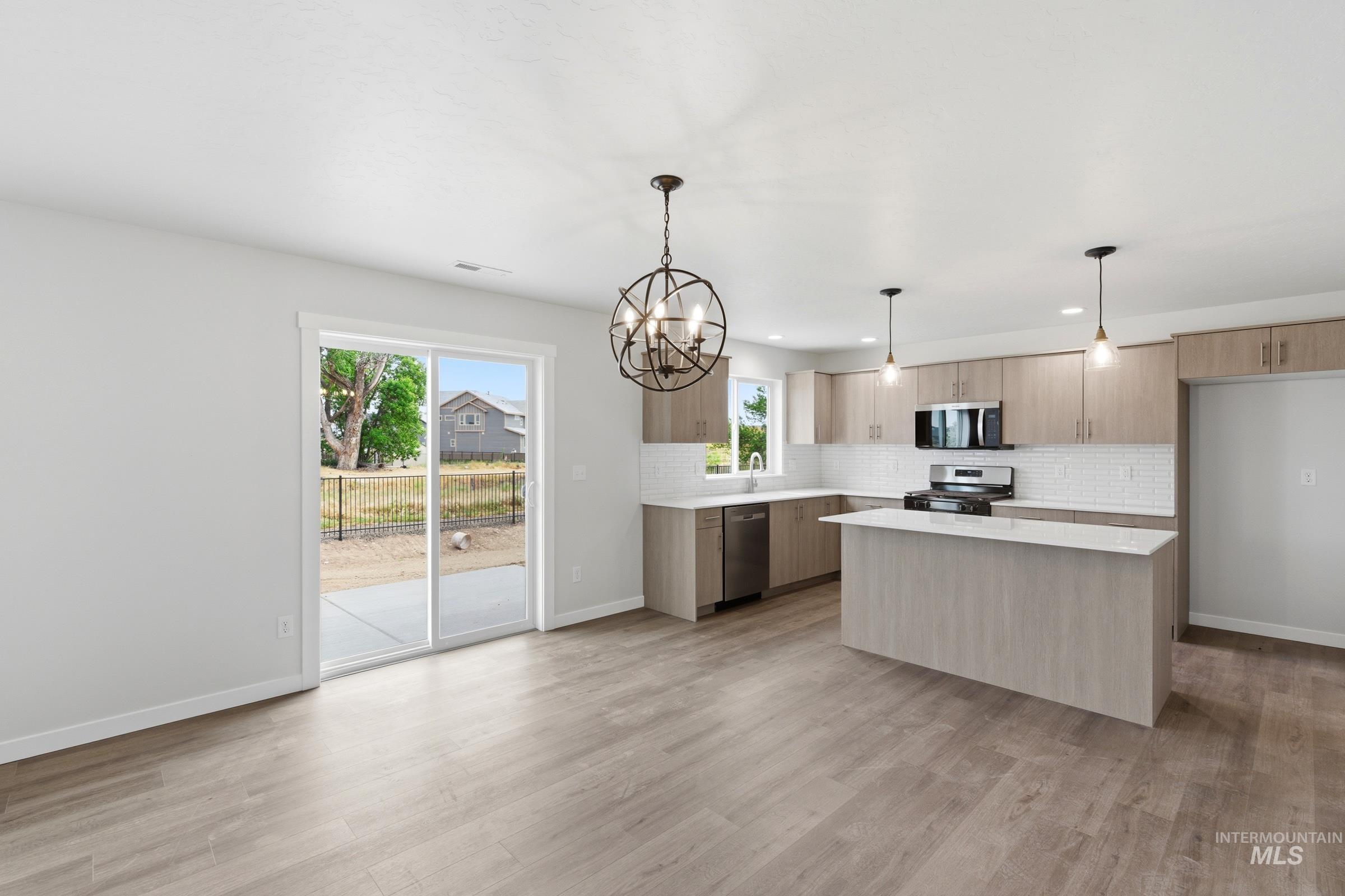 12829 Decatur Street Nampa, ID 83651 - Photo 7 of 33 Open-concept kitchen featuring light wood-finish cabinetry, a central island with a solid surface countertop, stainless steel appliances, and a white subway tile backsplash
