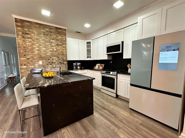 a kitchen with stainless steel appliances granite countertop a stove a refrigerator a sink a oven with white cabinets and wooden floor