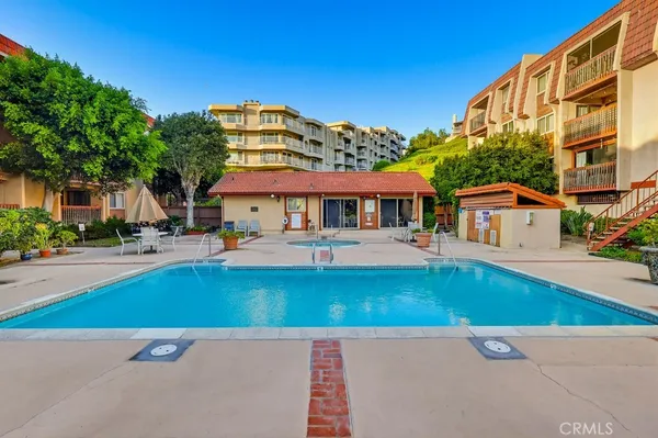a view of a white building with a swimming pool and lawn chairs under an umbrella