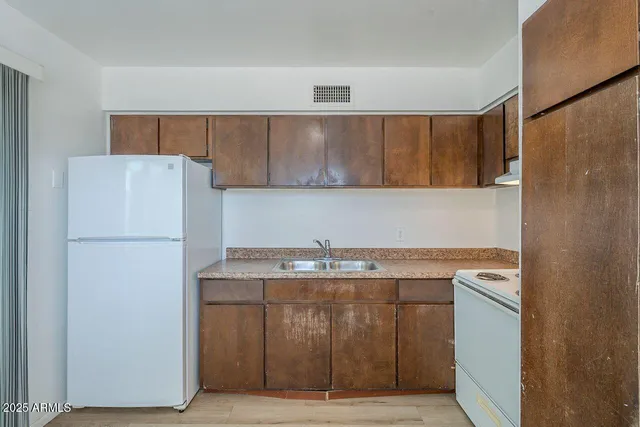 a kitchen with stainless steel appliances granite countertop a refrigerator a sink and white cabinets with wooden floor