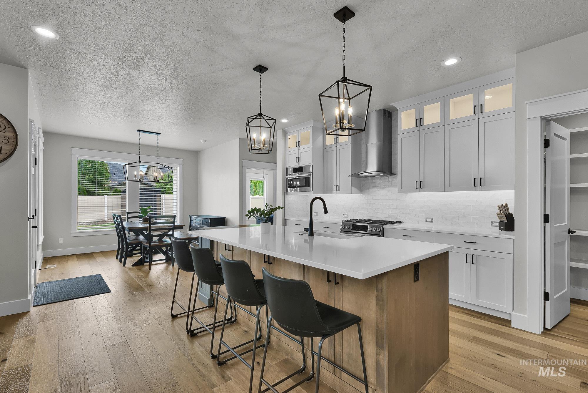 5676 East Zaffre Ridge Street Boise, ID 83716 - Photo 10 of 50 Expansive kitchen featuring a large central island with seating, light wood-finish flooring, white cabinetry with upper glass accents, stainless steel appliances, and a tiled backsplash