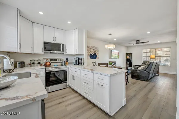 a large white kitchen with stainless steel appliances granite countertop a stove oven a sink dishwasher and white cabinets with wooden floor