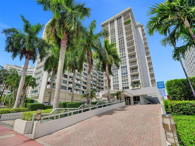 a front view of a residential apartment building with a yard and palm trees