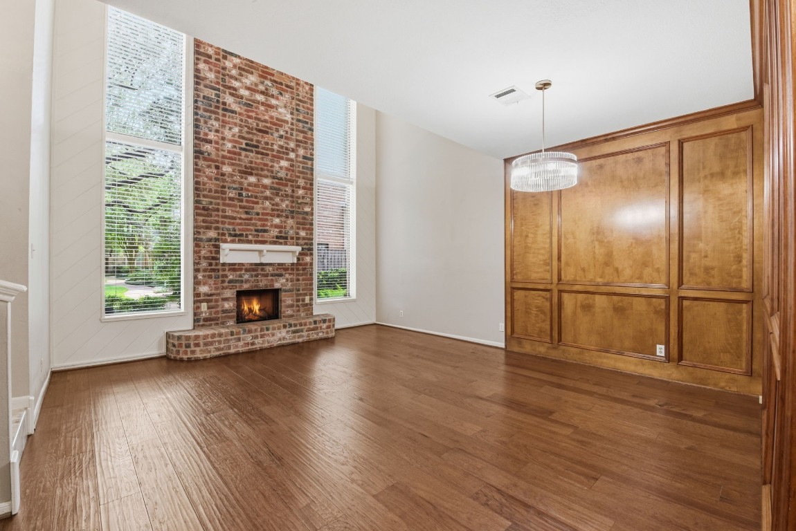 727 Bunker Hill Road, Unit 34 Houston, TX 77024 - Photo 6 of 50 Grand living room with soaring two-story brick fireplace, floor-to-ceiling windows, rich hardwood floors, elegant wood-paneled wall, and beautiful chandelier