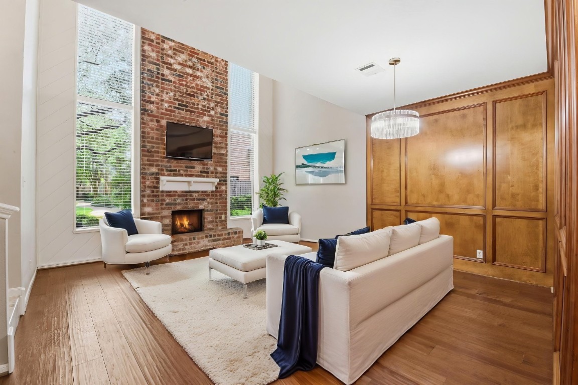 727 Bunker Hill Road, Unit 34 Houston, TX 77024 - Photo 7 of 50 Spacious living room with warm wood-paneled walls, brick fireplace, hardwood floors, and plenty of natural light (Virtually Staged)
