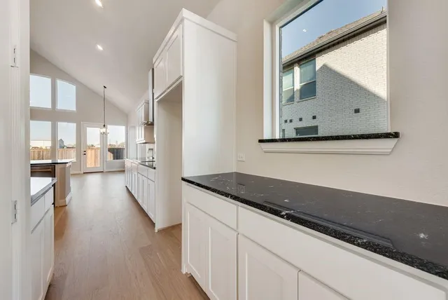 a kitchen with granite countertop a refrigerator a stove and white cabinets with wooden floor