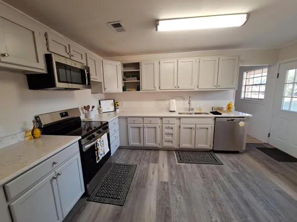 a kitchen with stainless steel appliances a sink dishwasher a stove top oven a refrigerator with wooden floor and cabinets