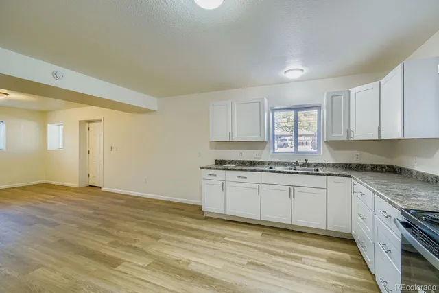 a kitchen with granite countertop a stove a sink and white cabinets