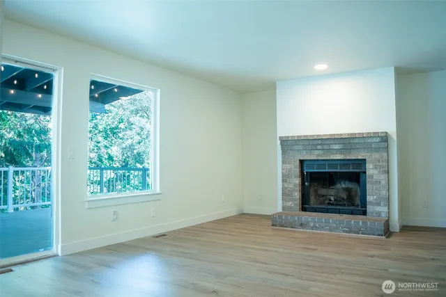 a view of an empty room with wooden floor fireplace and a window