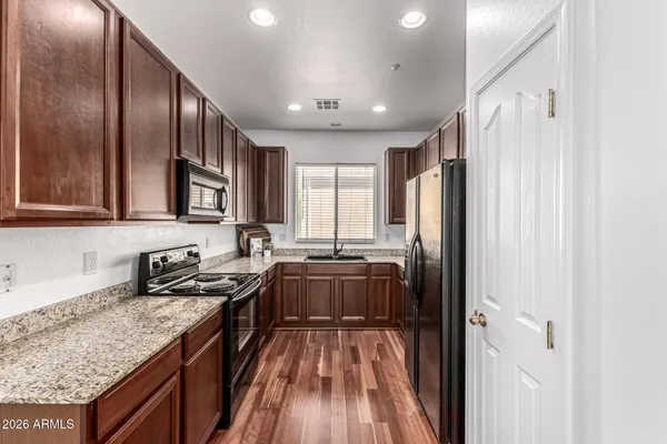 a kitchen with stainless steel appliances granite countertop a refrigerator a sink dishwasher a stove and white countertops with wooden floor