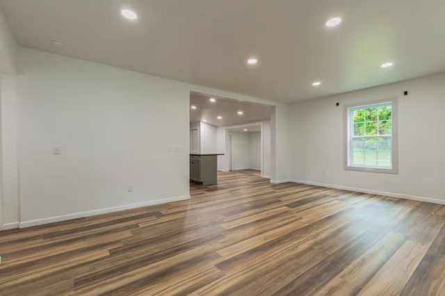 a view of empty room with wooden floor and kitchen