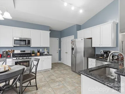 a kitchen with stainless steel appliances granite countertop a sink a stove a refrigerator and white cabinets