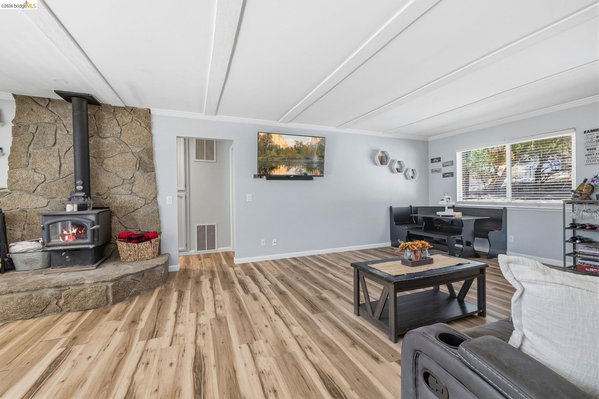 19059 Raboul Court Groveland, CA 95321 - Photo 8 of 21 Living area featuring a stone accent wall, wood-burning stove, wood-finish flooring, and a dining nook with exterior window