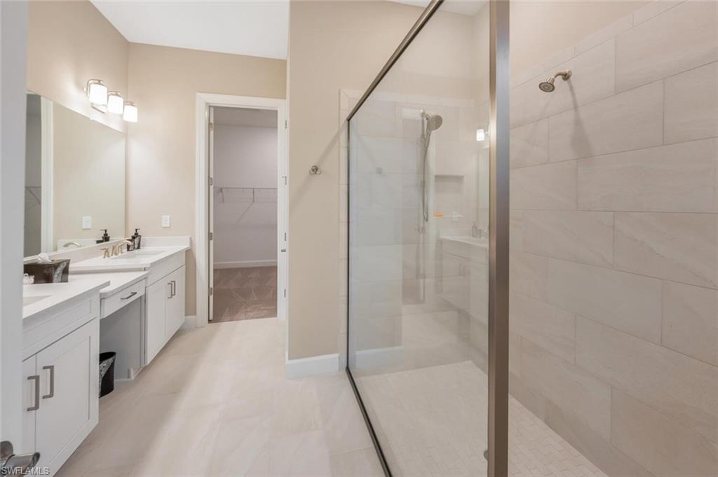 8448 Rosa Court Naples, FL 34114 - Photo 16 of 24 Spacious bathroom featuring a frameless glass shower enclosure, large format wall tiling, dual vanity with white cabinetry, light-toned countertop, and tile flooring