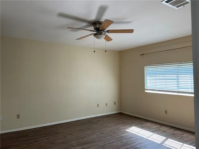an empty room with wooden floor fan and windows