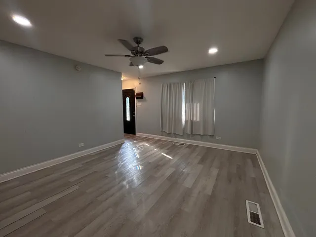 an empty room with wooden floor fan and windows