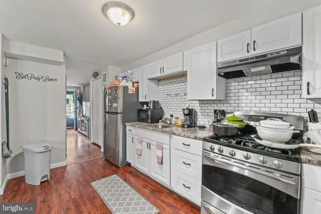 a kitchen with stainless steel appliances a stove a sink a refrigerator cabinets and wooden floor