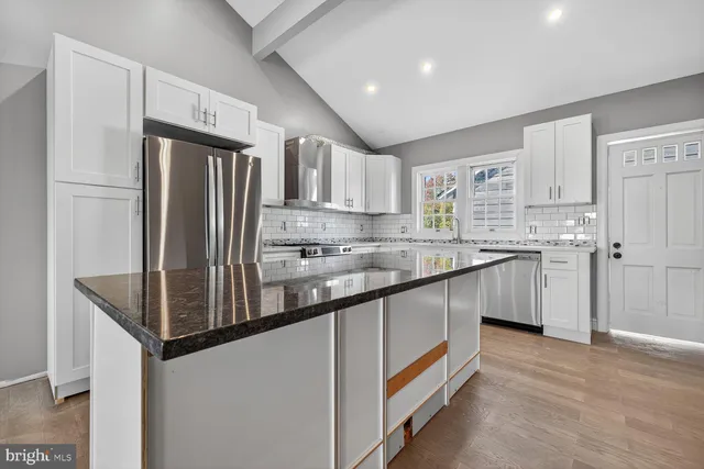 a kitchen with stainless steel appliances granite countertop a refrigerator a sink dishwasher a stove and white countertops with wooden floor