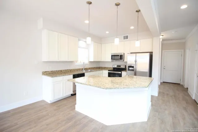 a kitchen with stainless steel appliances granite countertop a sink a stove a refrigerator and island with wooden floor