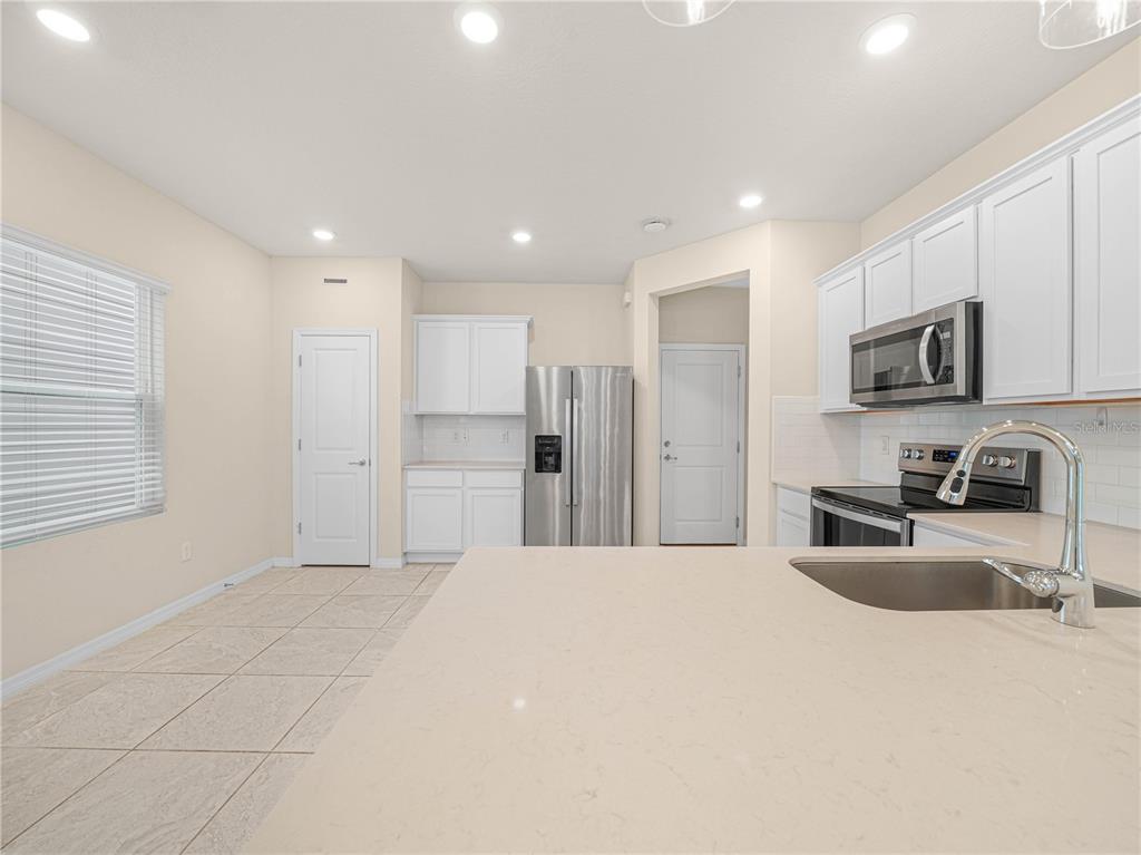 4580 Sparkling Shell Avenue Kissimmee, FL 34746 - Photo 19 of 42 a large kitchen with kitchen island granite countertop a sink a stove a refrigerator a window and white cabinets