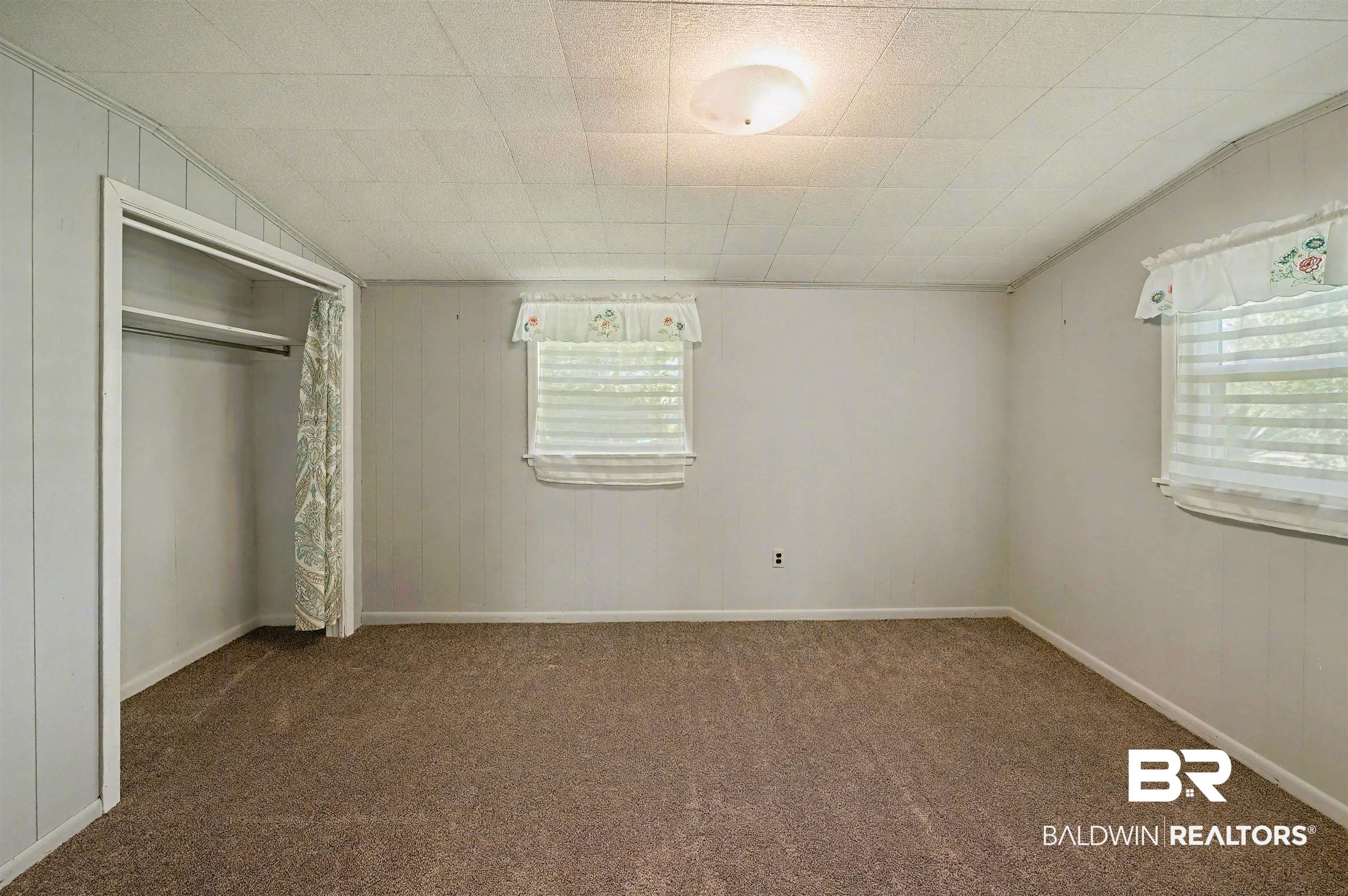 209 West Magnolia Avenue Foley, AL 36535 - Photo 14 of 23 Unfurnished bedroom featuring lofted ceiling, dark carpet, wooden walls, and a closet