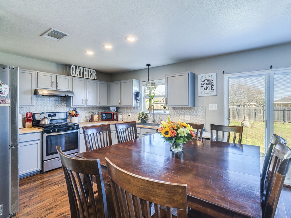 13021 Maidenhair Trail Elgin, TX 78621 - Photo 7 of 25 a kitchen with stainless steel appliances granite countertop a stove a refrigerator a dining table and chairs