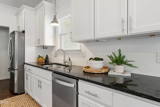 a kitchen with stainless steel appliances granite countertop white cabinets a sink and a potted plant