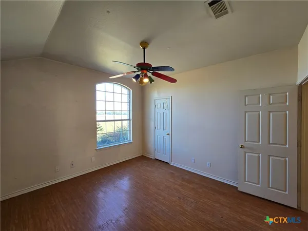 an empty room with wooden floor fan and windows