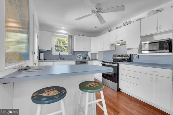 a kitchen with stainless steel appliances granite countertop a sink a stove a refrigerator cabinets and a dining table with wooden floor