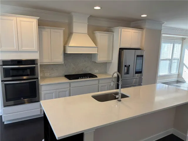 a large kitchen with stainless steel appliances a large counter top a stove a sink and a refrigerator