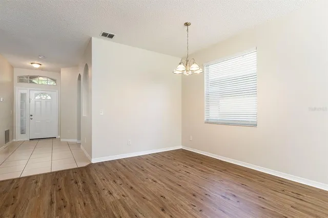 an empty room with wooden floor chandelier and windows