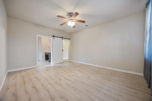 a view of an empty room with wooden floor and a ceiling fan