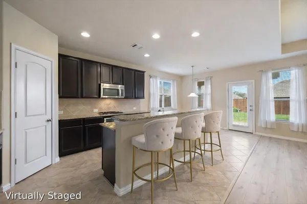 a kitchen with stainless steel appliances granite countertop a stove a sink a refrigerator a dining table and chairs