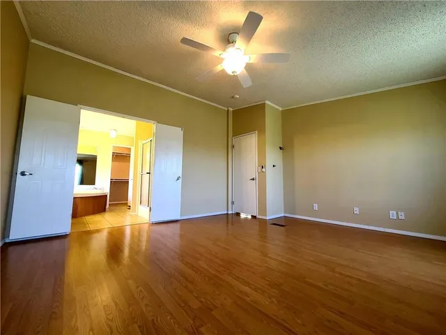 a view of an empty room with wooden floor and a ceiling fan