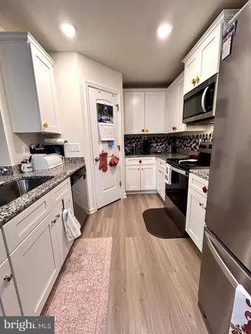 a kitchen with stainless steel appliances kitchen island granite countertop a refrigerator a sink dishwasher a stove and white cabinets with wooden floor