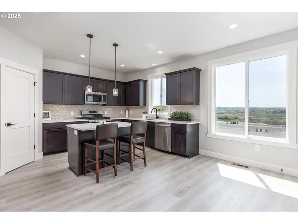a kitchen with stainless steel appliances kitchen island granite countertop a refrigerator a stove a sink a dining table and chairs with wooden floor