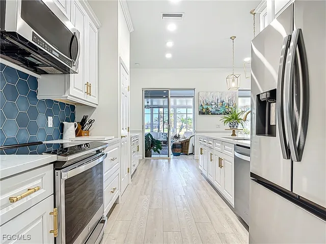 a kitchen with stainless steel appliances a stove a sink dishwasher a refrigerator white cabinets and wooden floor