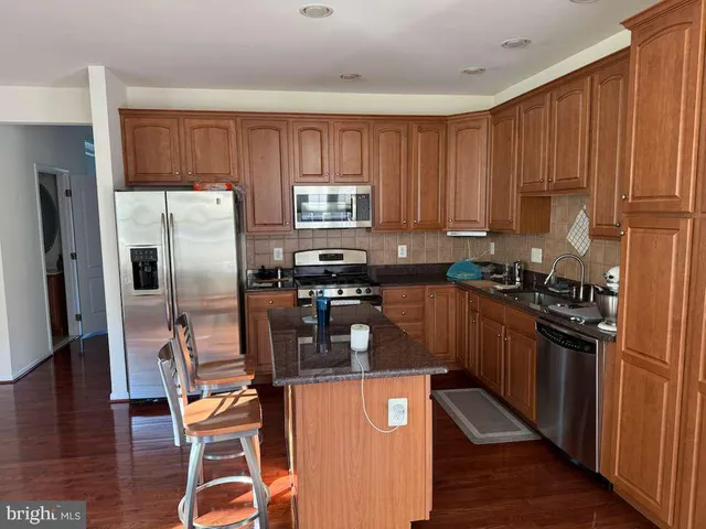 a kitchen with granite countertop a refrigerator stove top oven and wooden floor
