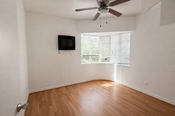 an empty room with wooden floor fan and windows